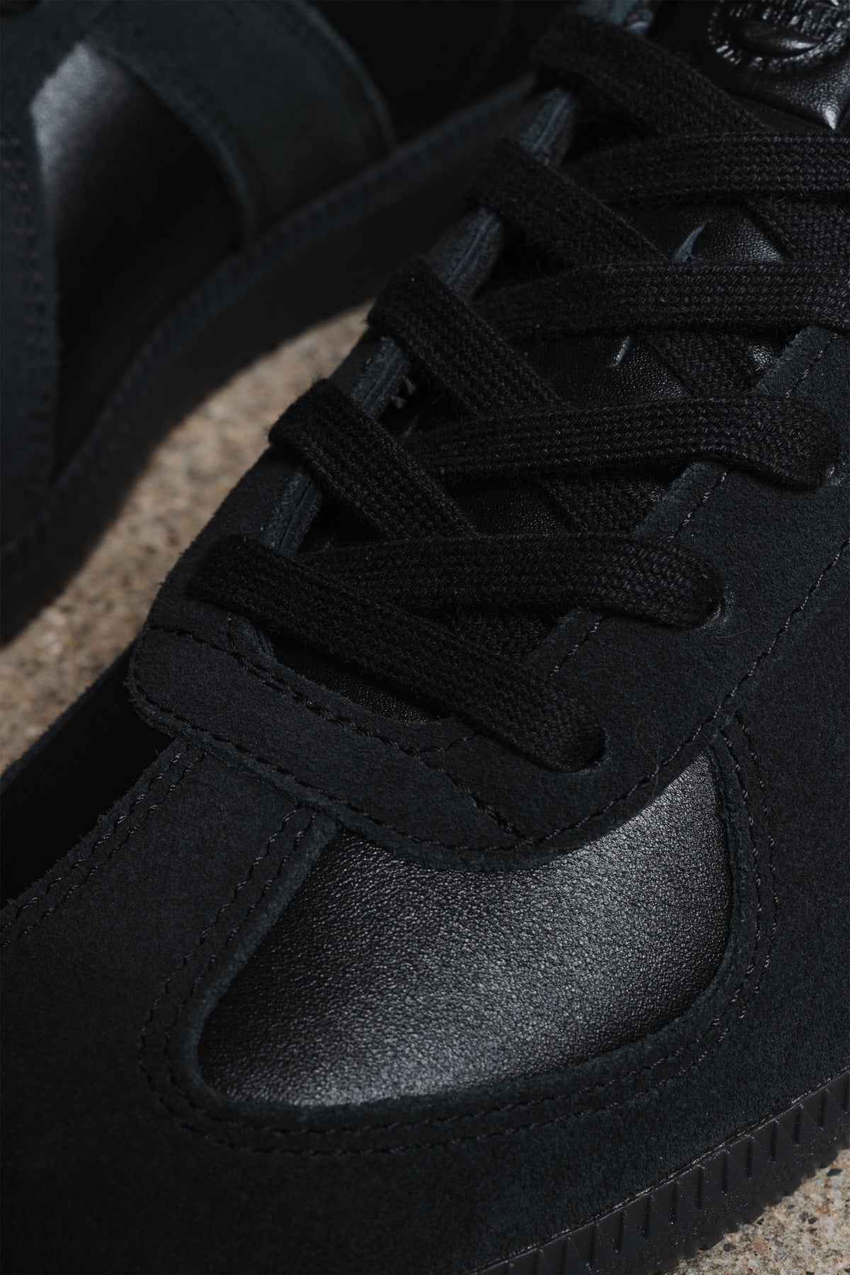 Close-up of a black suede and leather sneaker with black laces, showing the textured toe box and side panel details.